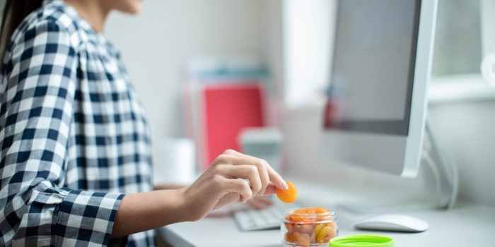 Female Worker In Office Having Healthy Snack Of Dried Apricots At Desk